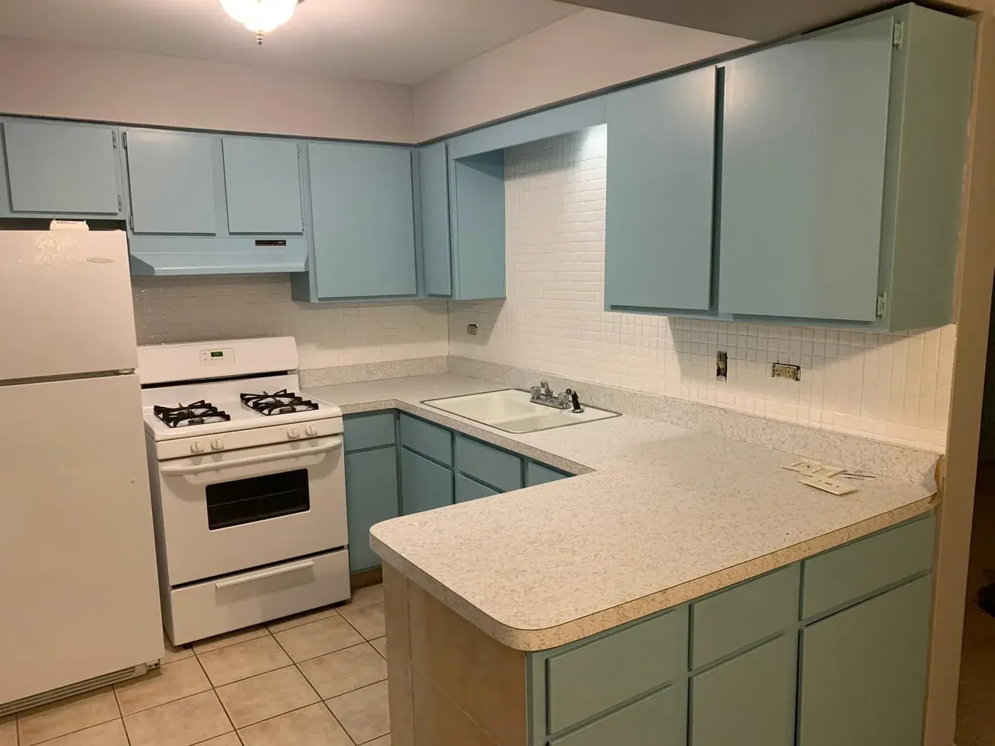 Kitchen before refinishing, dated teal cabinets and a beige counter