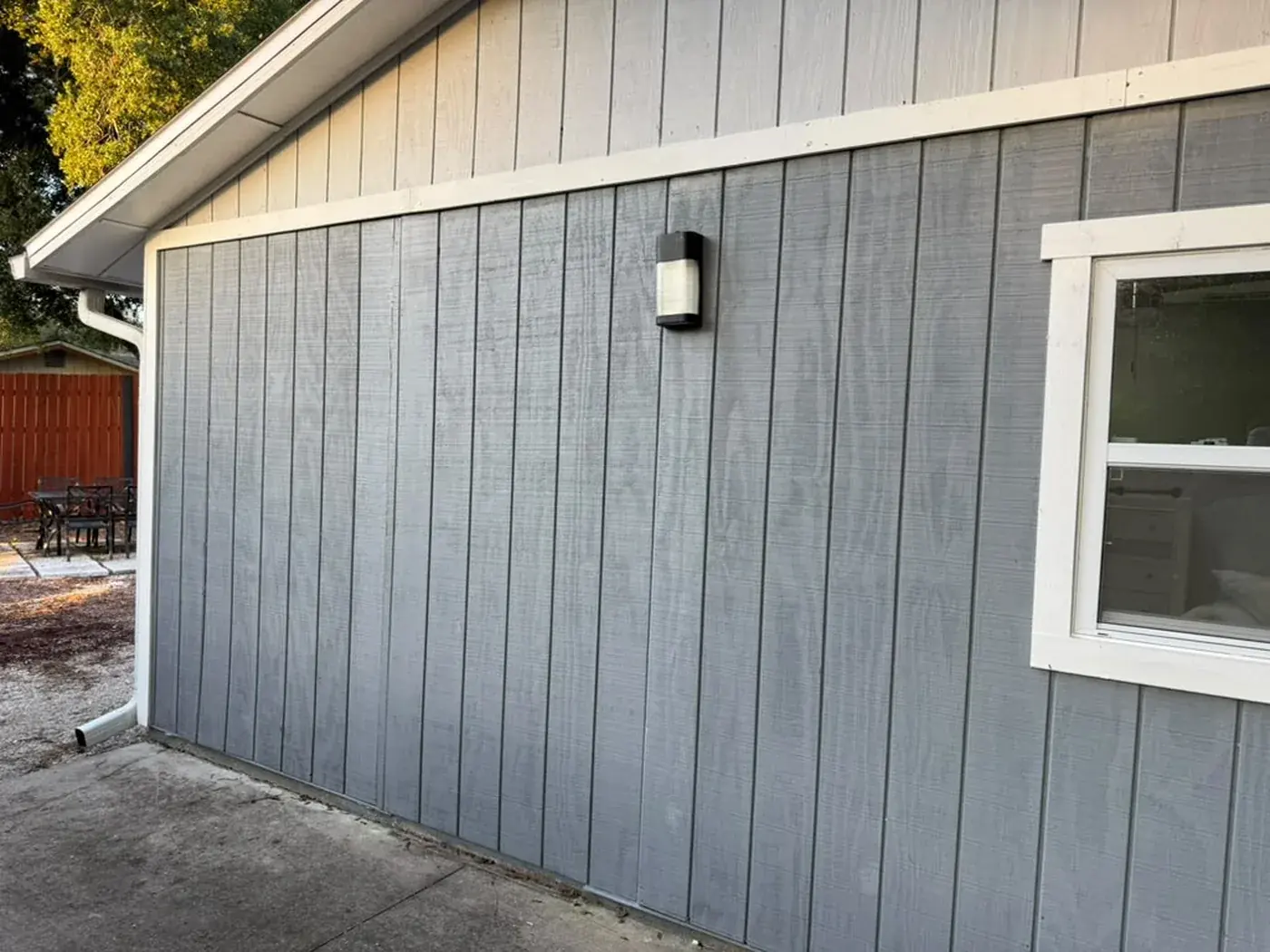 Board and batten siding in pale grey before repainting, white trim and gutter