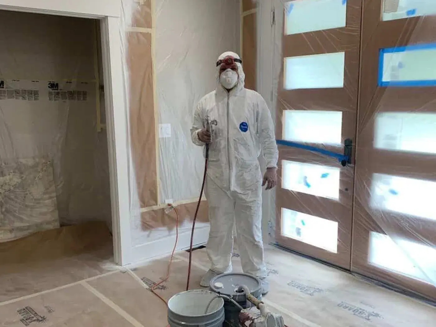 Painter in a full protective suit with the spray rig, entry hall masked floor to ceiling