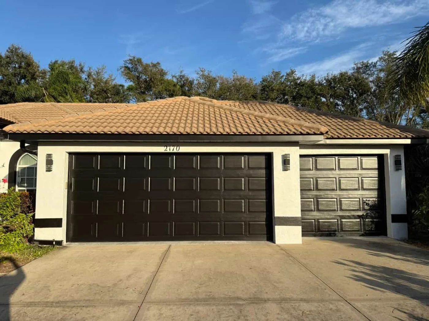 Two garage doors finished in deep brown against cream stucco and a tile roof