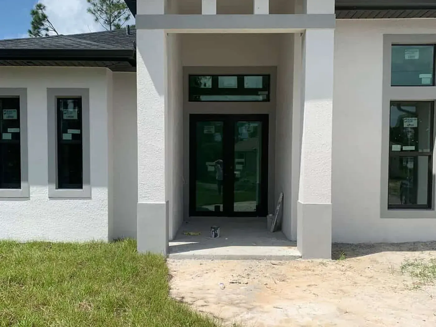 Modern entry with pale columns and black glazed doors, stucco freshly coated