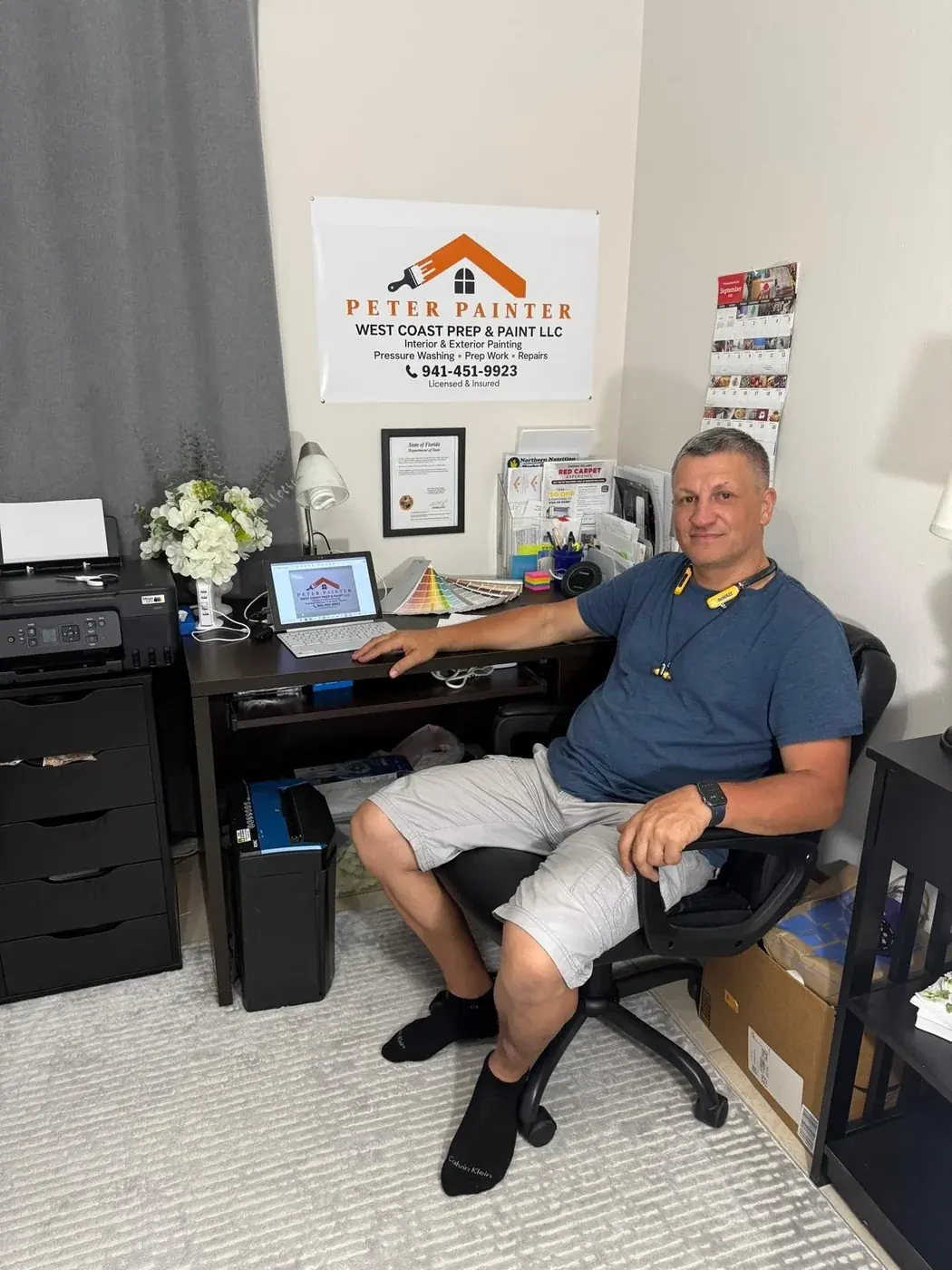 Piter Bulla at his desk under the West Coast Prep and Paint banner